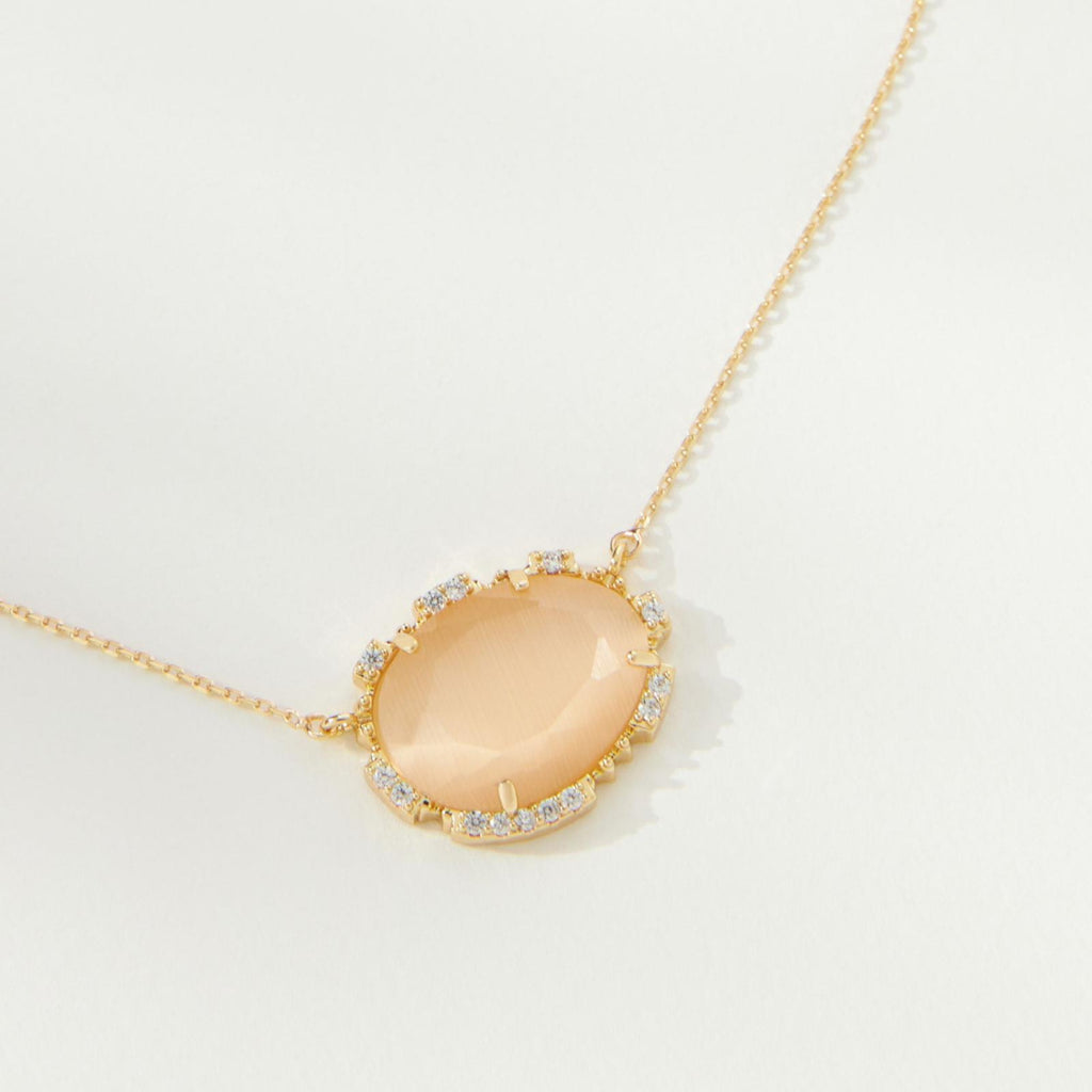 Gold necklace with a peach-colored pendant on a light gray background