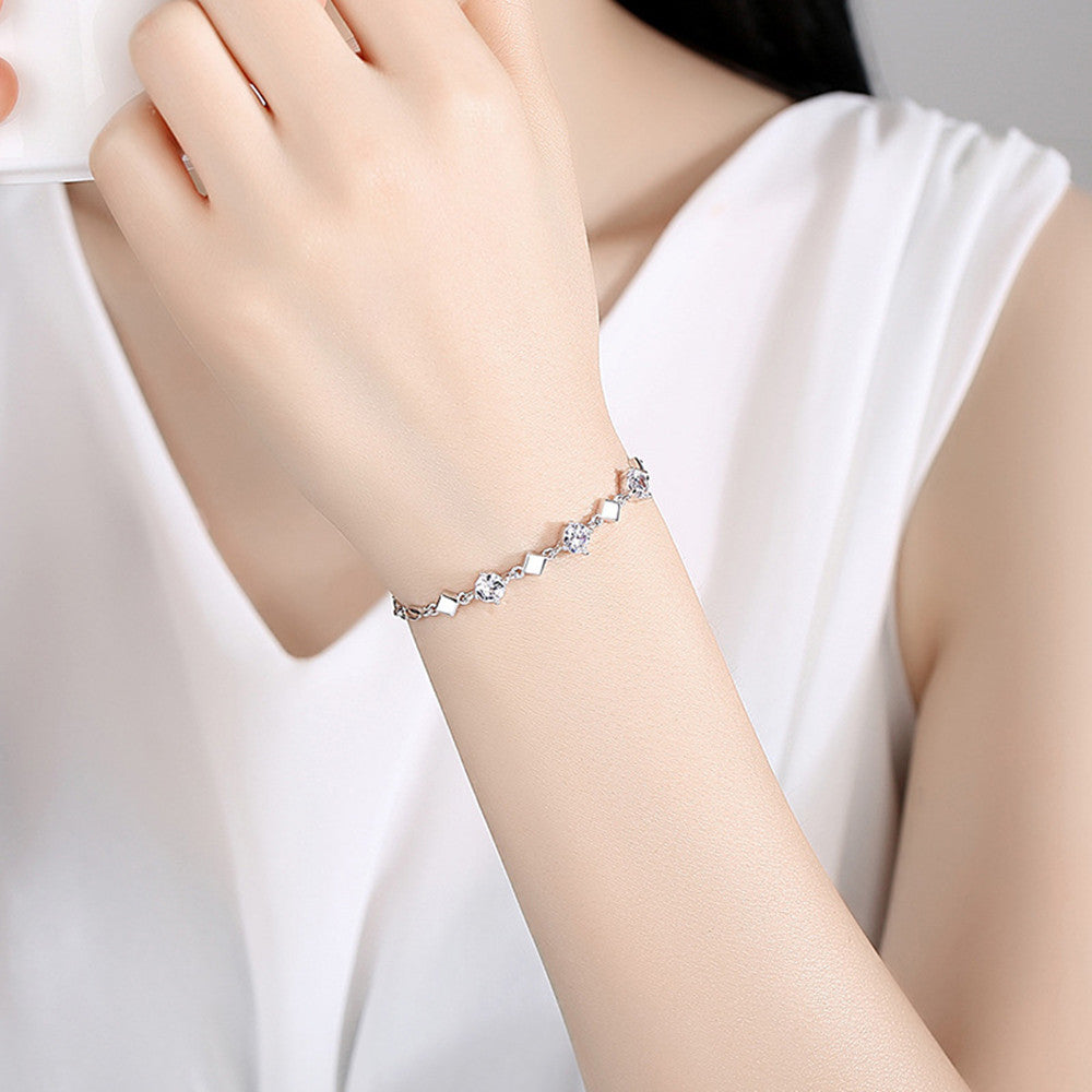 Hand wearing a silver bracelet with small stones on a plain background