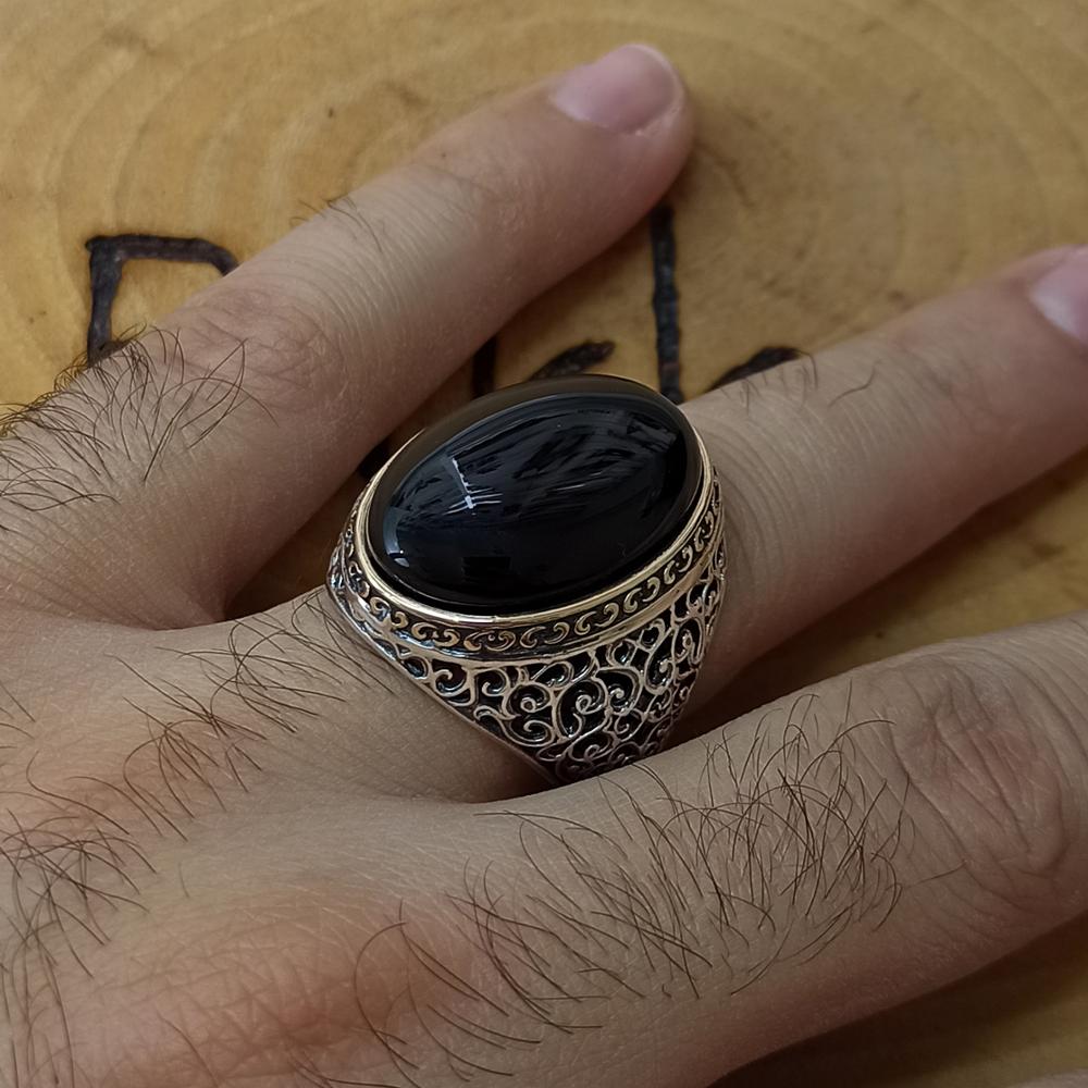 Hand wearing a decorative ring with a black stone on a wooden background