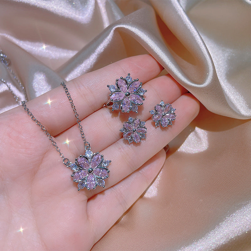 Flower-shaped pink gemstone jewelry set on a hand with a satin background