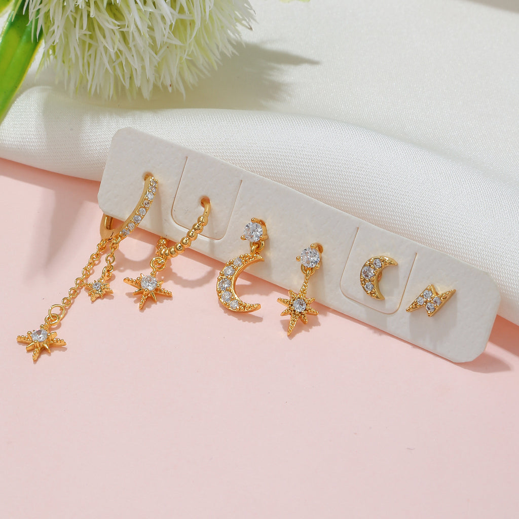 Gold earrings with star and moon designs on a pink surface