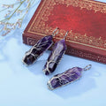 Three purple crystal pendants on a light blue surface with an ornate red book in the background.