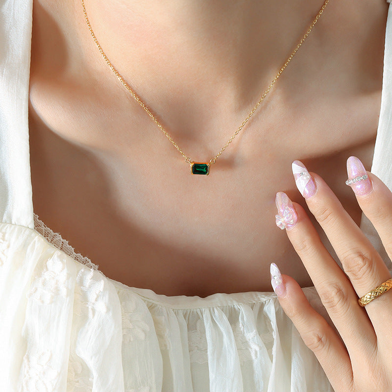 Gold necklace with a green gemstone worn by a person, with a hand touching the necklace.