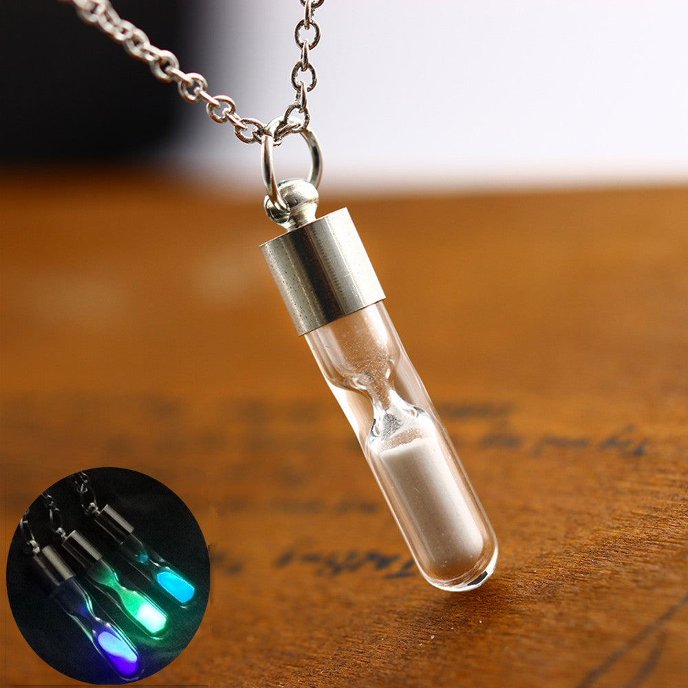 Glass vial necklace with chain on a wooden surface, glowing in dark setting.