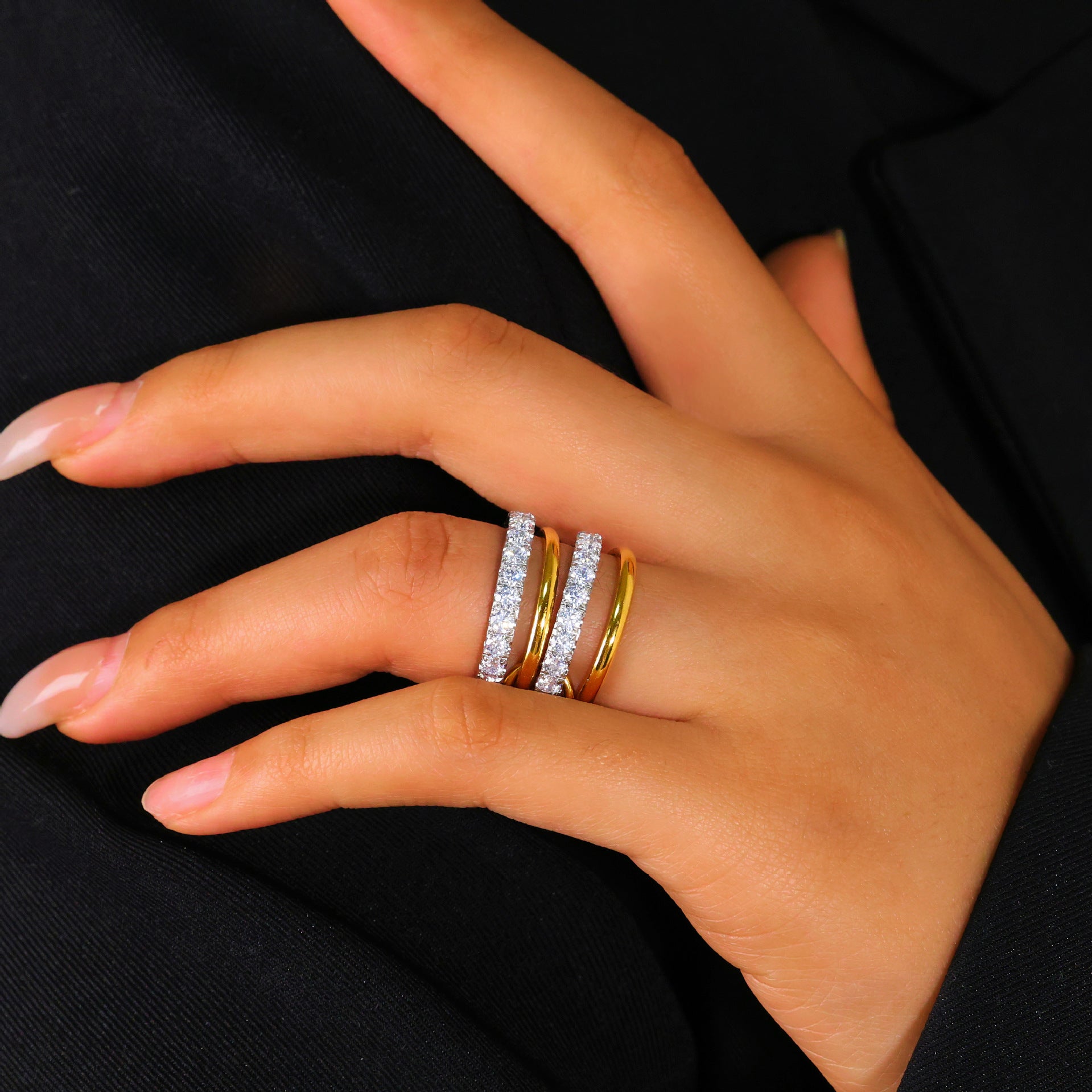Hand wearing two gold rings on a black background