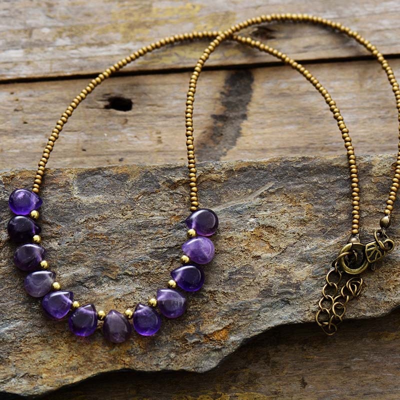 Necklace with purple beads and gold accents on a stone surface