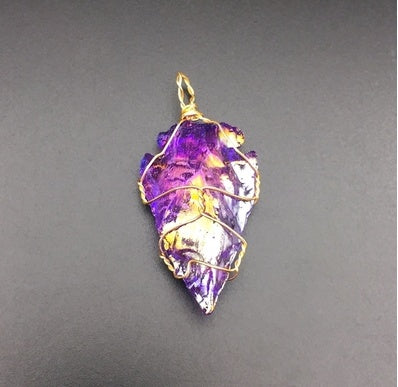 Purple gemstone pendant with gold wire wrapping on a gray background
