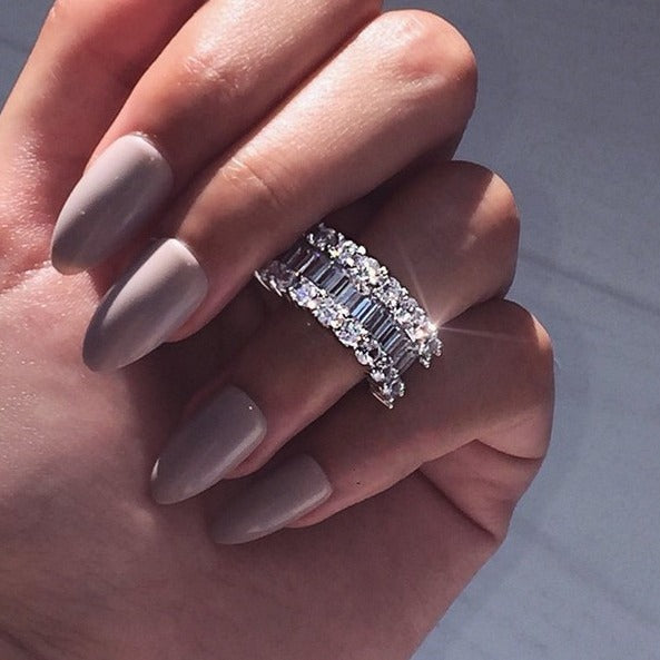 Hand with gray nail polish wearing a decorative ring on a neutral background