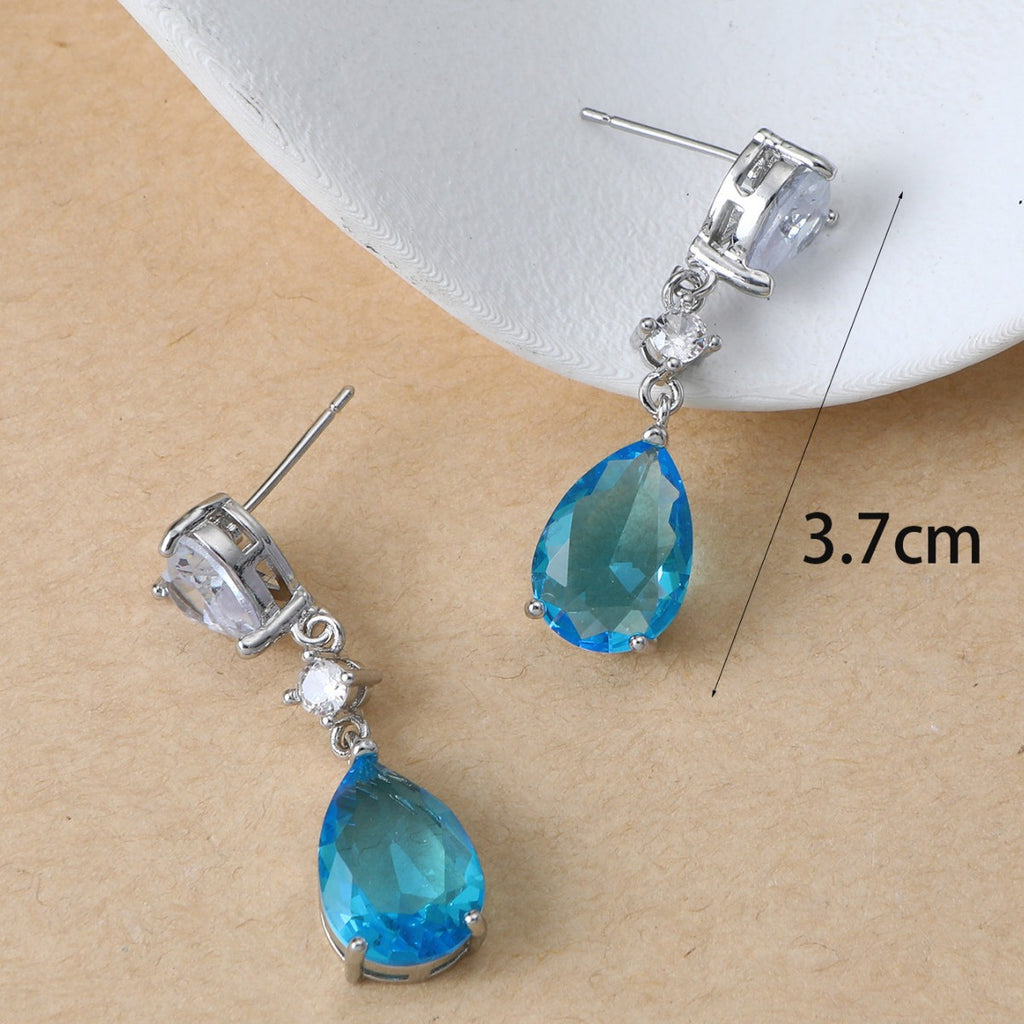 Blue teardrop earrings with silver accents on a beige background