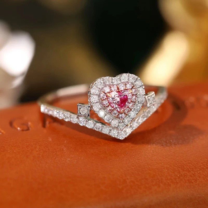 Heart-shaped diamond ring with a pink gemstone on an orange surface