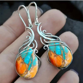 Silver earrings with turquoise and orange stones held in a hand against a dark background