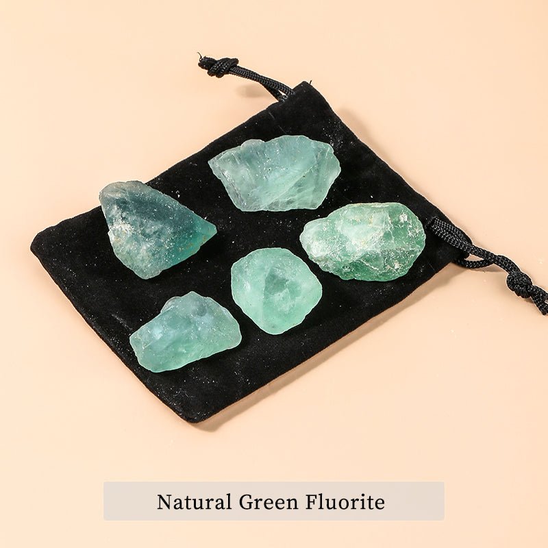 Five natural green fluorite crystals on a black drawstring bag against a beige background.