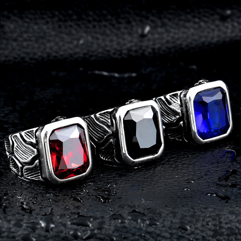 Three rings with red, black, and blue gemstones on a dark textured surface
