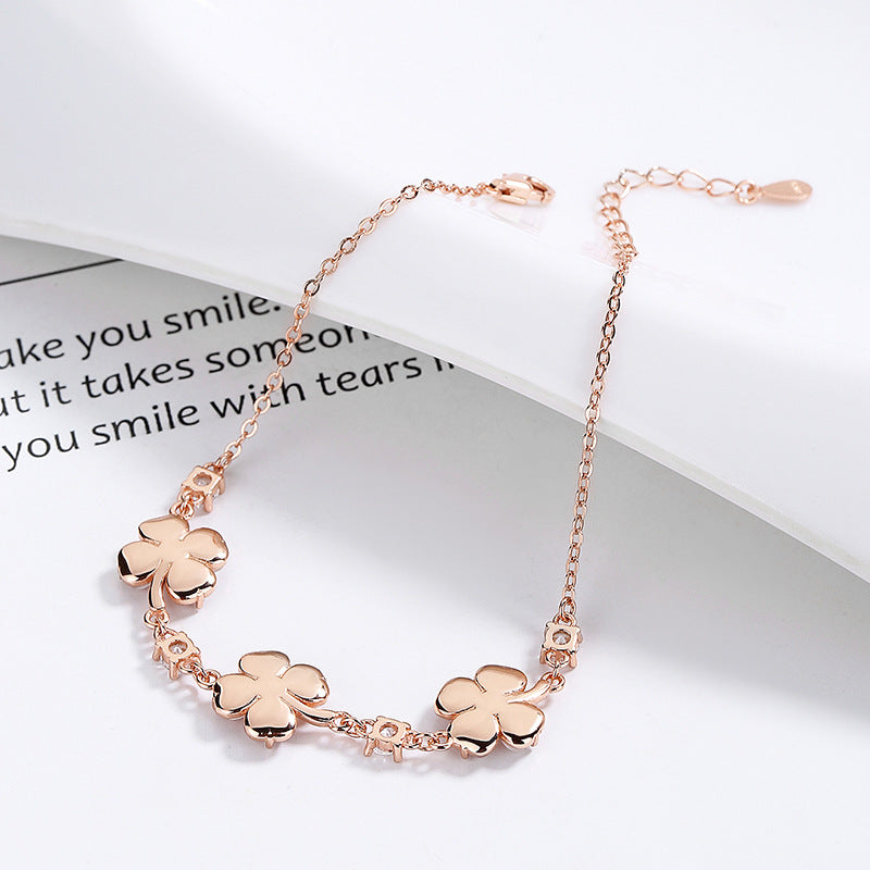 Rose gold bracelet with clover-shaped charms on a white surface