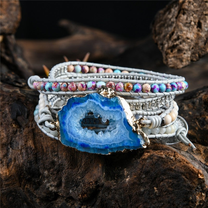 Stack of bracelets with a blue geode pendant on a wooden surface