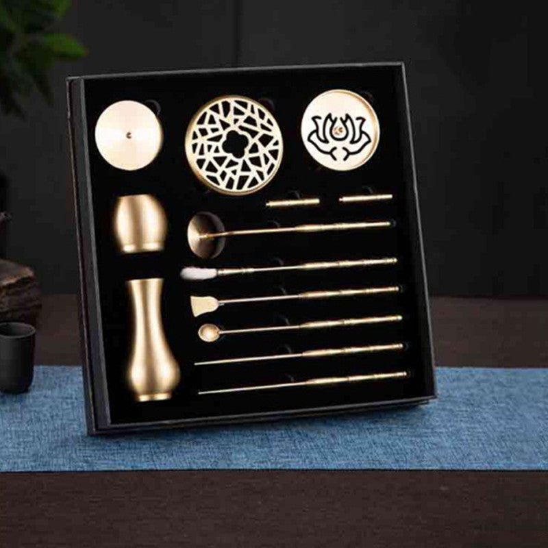 Set of gold tea accessories in a black box on a dark surface with a blue mat.
