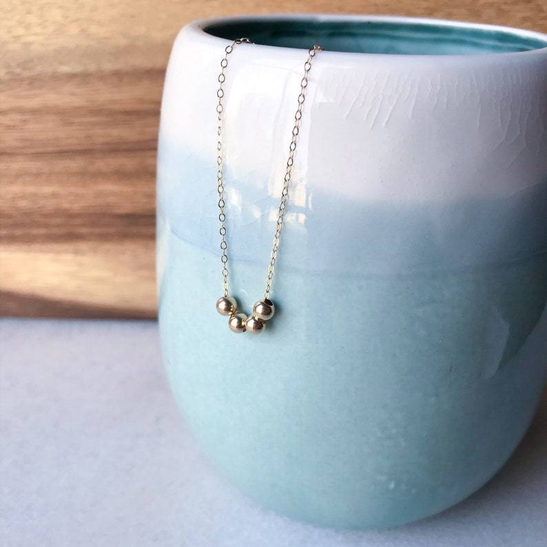 Gold necklace with three beads on a light blue ceramic cup