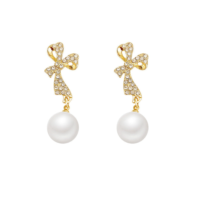 Gold bow-shaped earrings with pearl drops on a white background