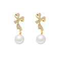 Gold bow-shaped earrings with pearl drops on a white background
