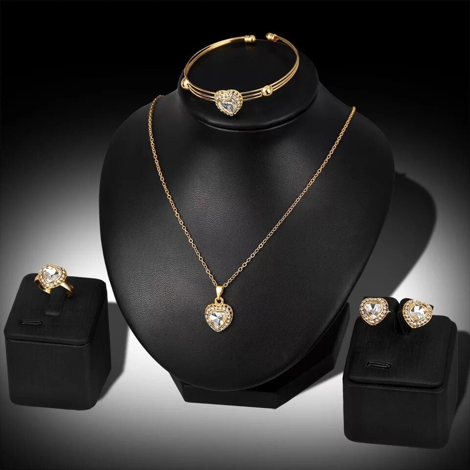 Gold jewelry set including necklace, ring, and earrings on a black stand with a dark background.