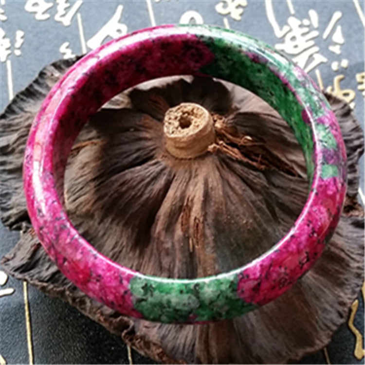 Green and pink bangle on a textured surface with blurred text in the background