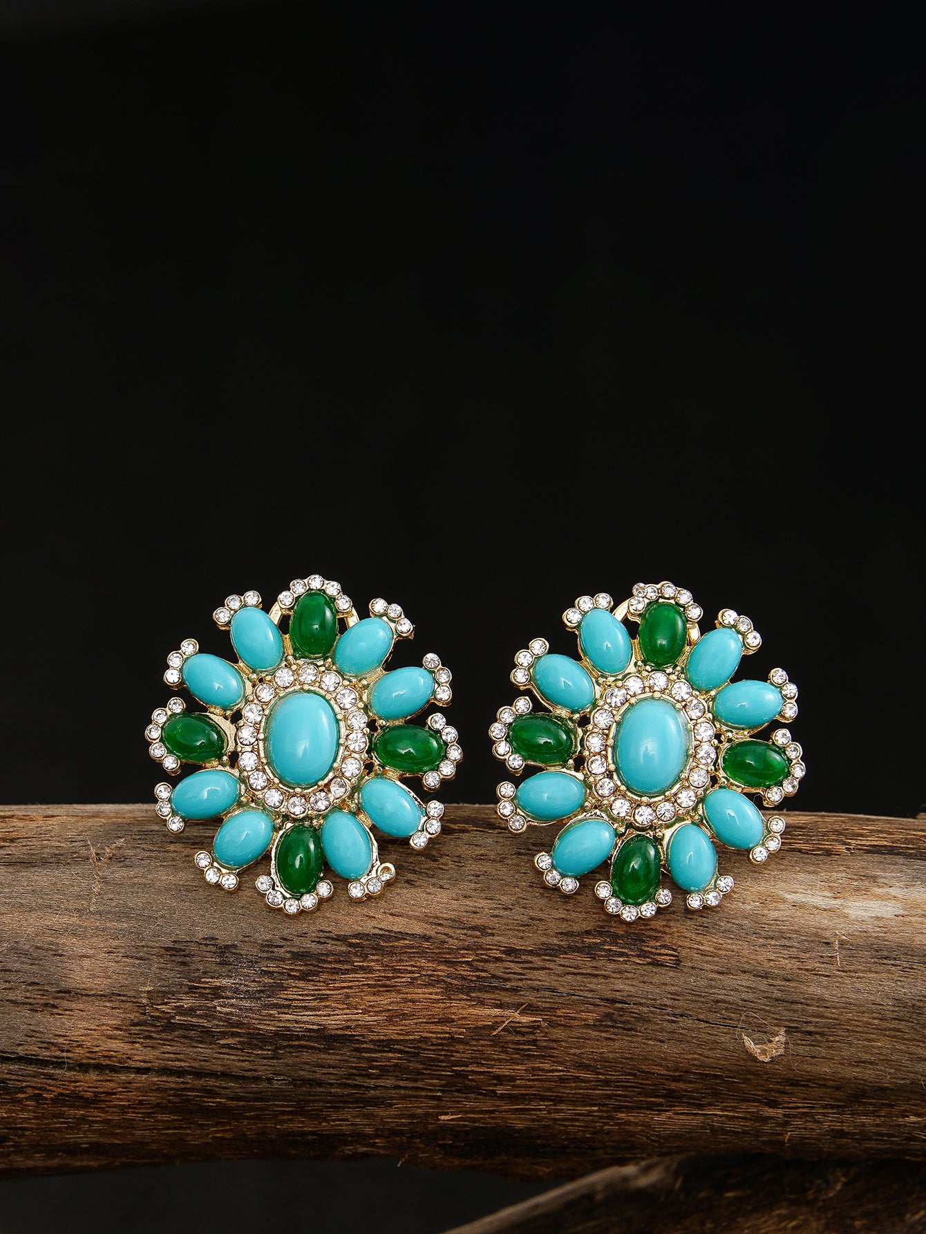 Pair of floral earrings with turquoise and green stones on a dark background