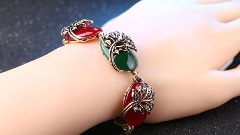 Bracelet with red and green stones on a wrist against a dark background