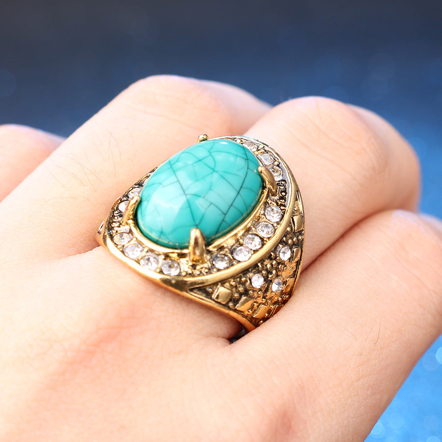 Gold ring with a turquoise stone on a hand against a blue background