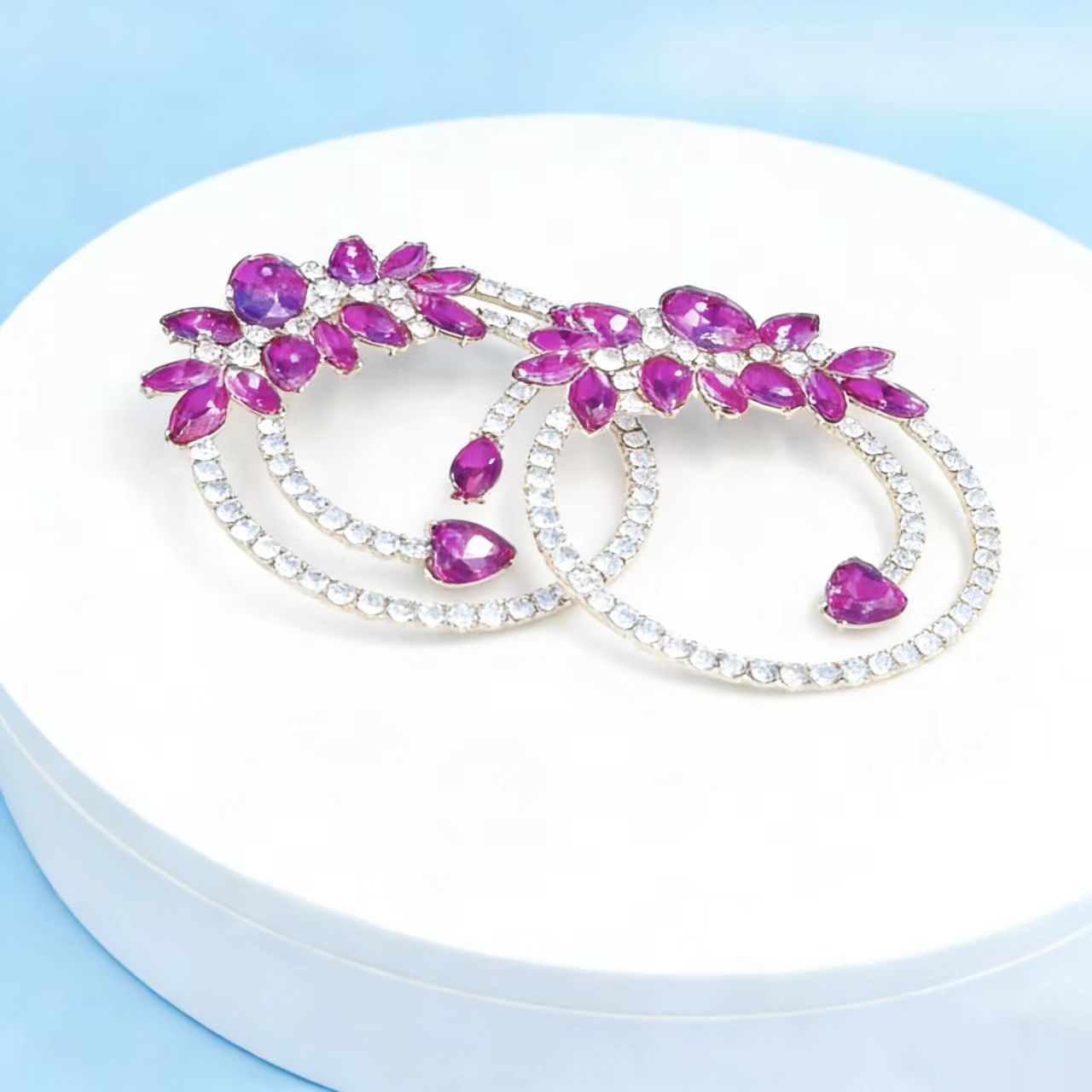 Pair of hoop earrings with purple gemstones on a white stand against a light blue background