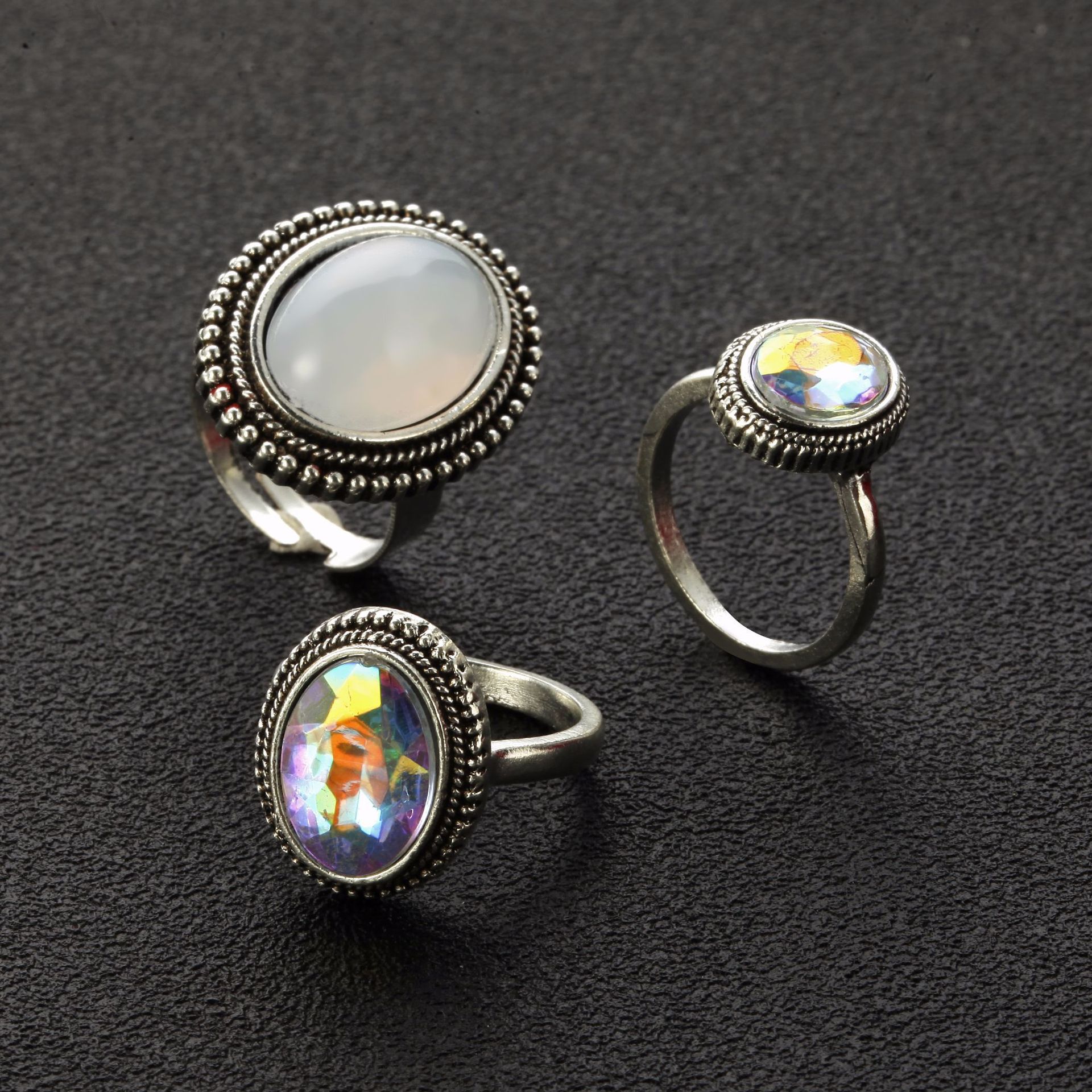 Three silver rings with gemstone-like inserts on a dark textured background