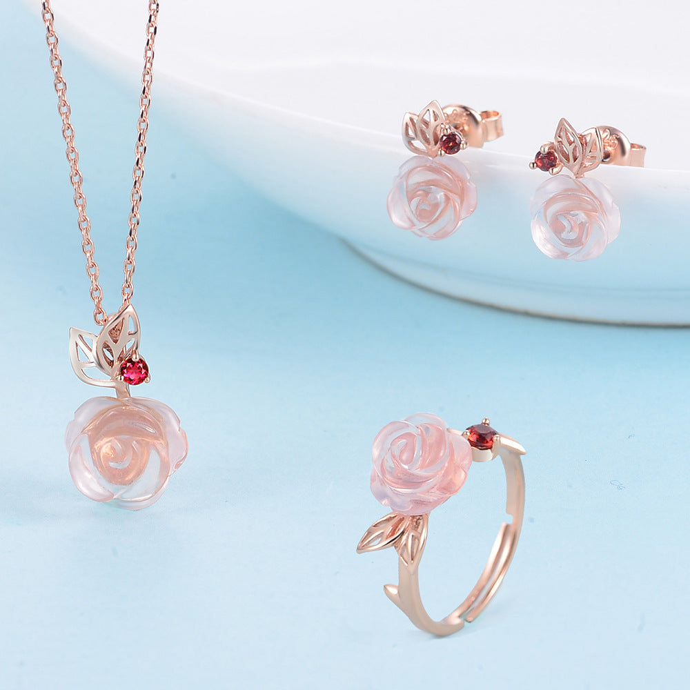 Rose gold jewelry set with pink rose designs on a light blue background