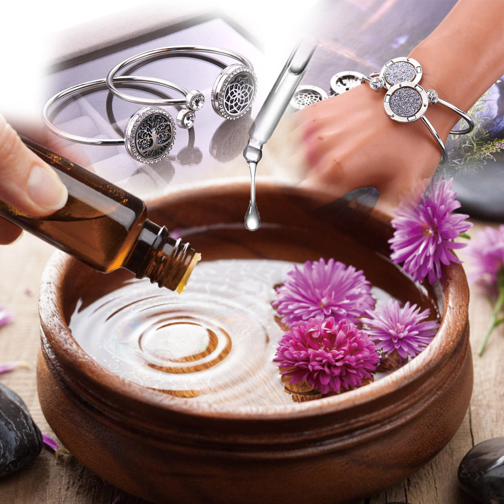 Bowl with water and flowers, bottle of oil, and silver bracelets on a wooden surface.