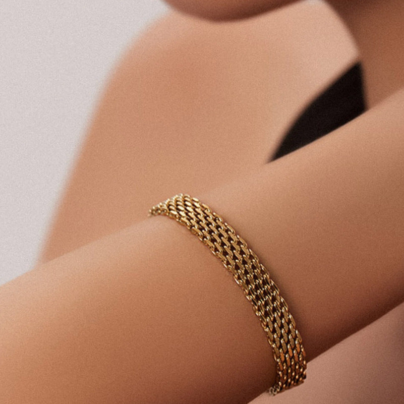 Gold bracelet on a person's wrist against a neutral background