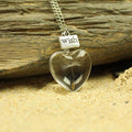 Heart-shaped pendant with a dandelion seed and 'Wish' tag on a wooden and sandy background