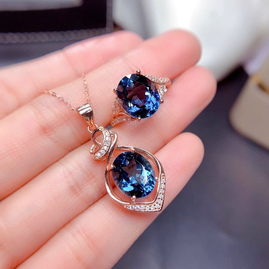 Two blue gemstone pendants on rose gold chains held in a hand.
