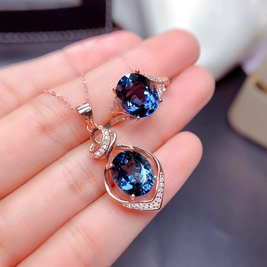Two blue gemstone pendants on rose gold chains held in a hand.