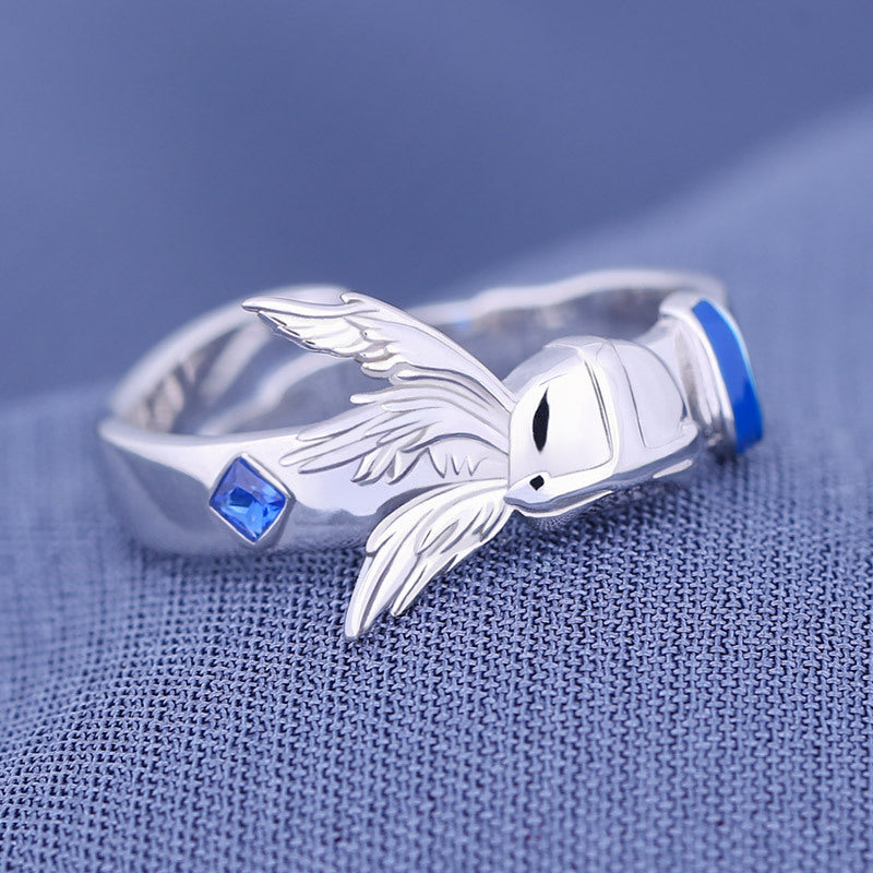Silver ring with angel wing design on a blue fabric background