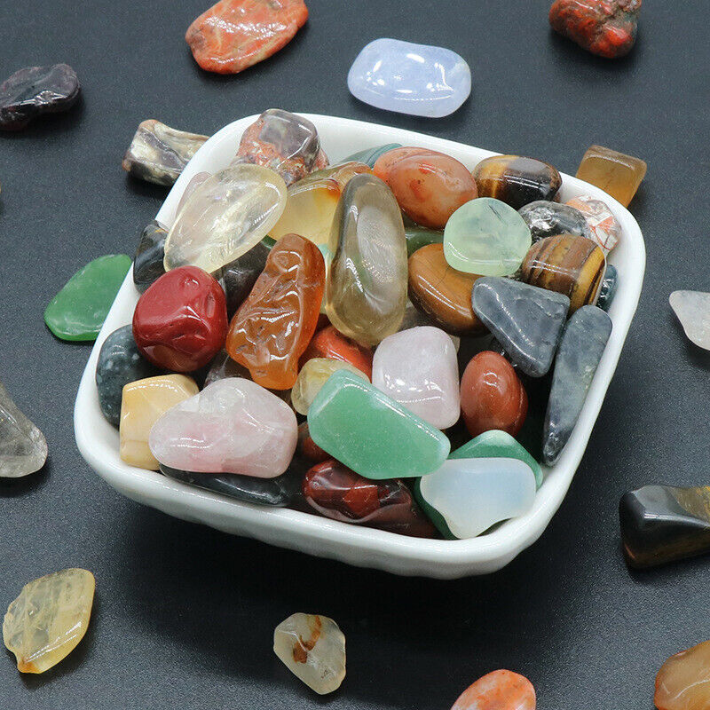 Assorted colorful gemstones in a white dish on a dark surface