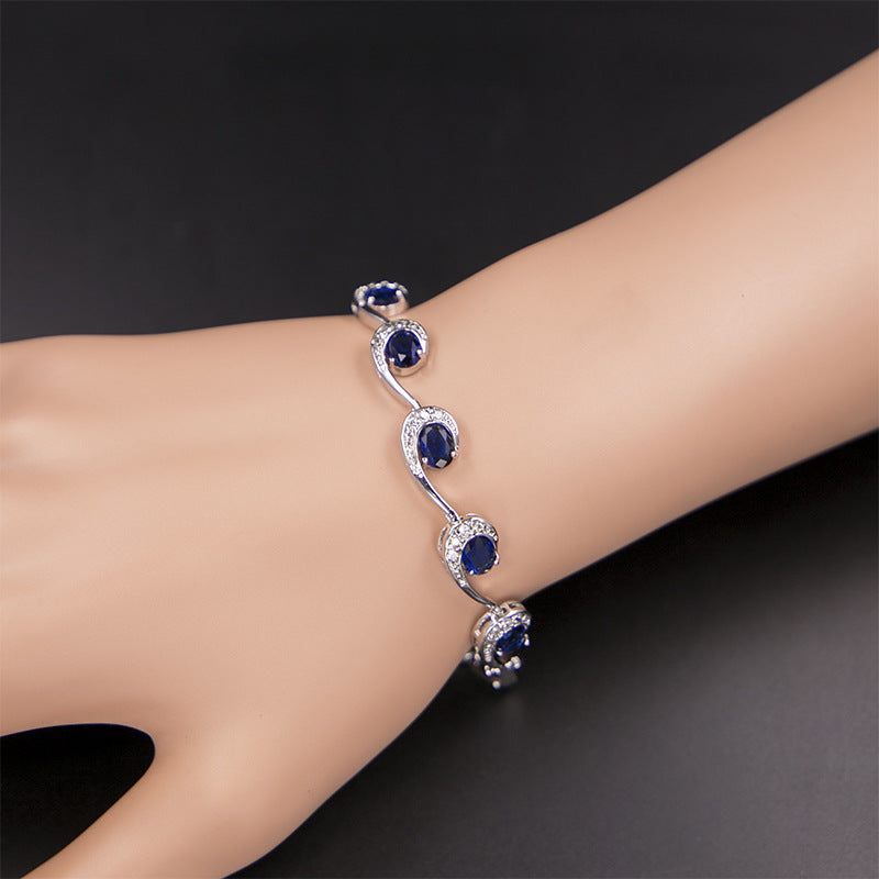 Silver bracelet with blue gemstones on a wrist against a dark background