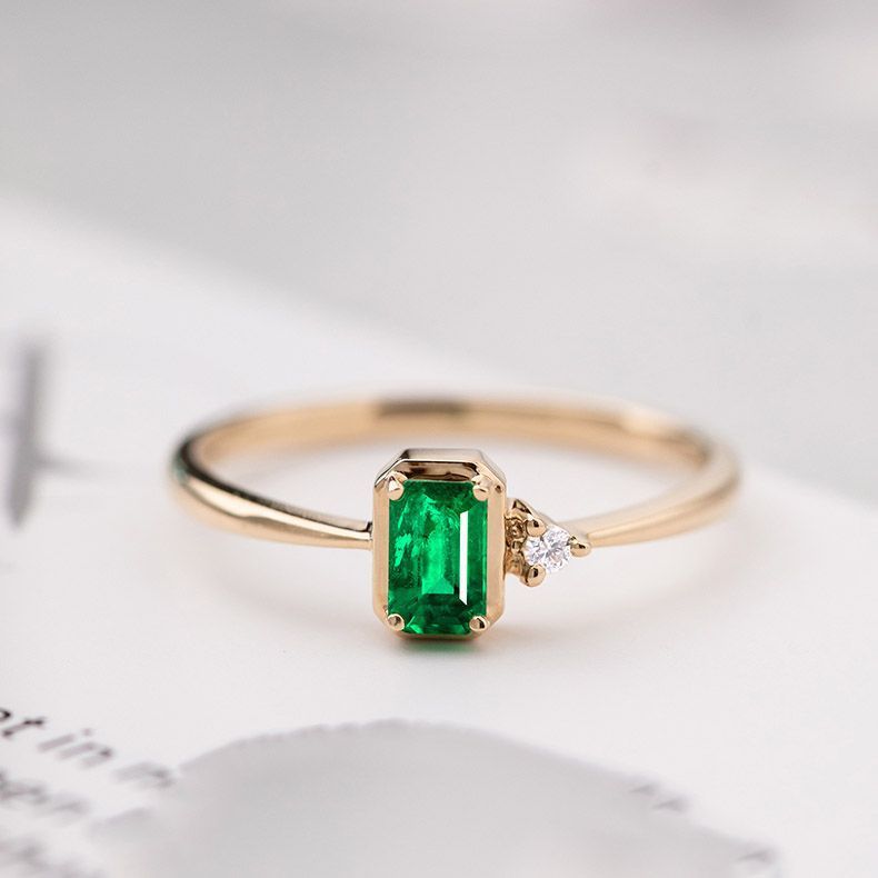 Gold ring with a green emerald stone on a light background
