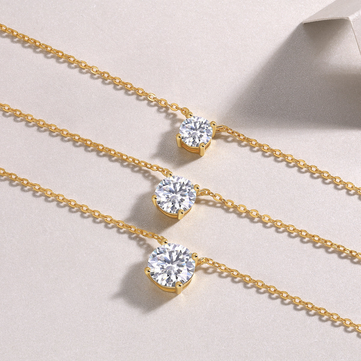 Three gold necklaces with diamond pendants on a light beige background