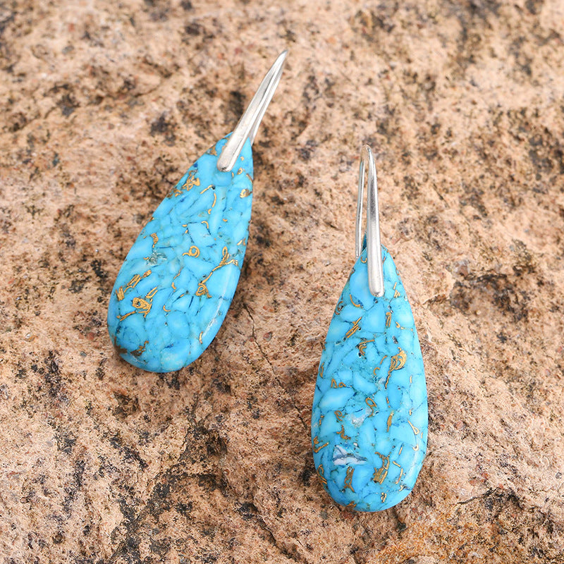 Turquoise teardrop earrings with gold specks on a brown stone surface