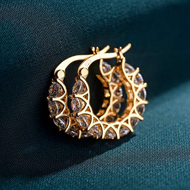 Gold hoop earrings with intricate design on a dark fabric background