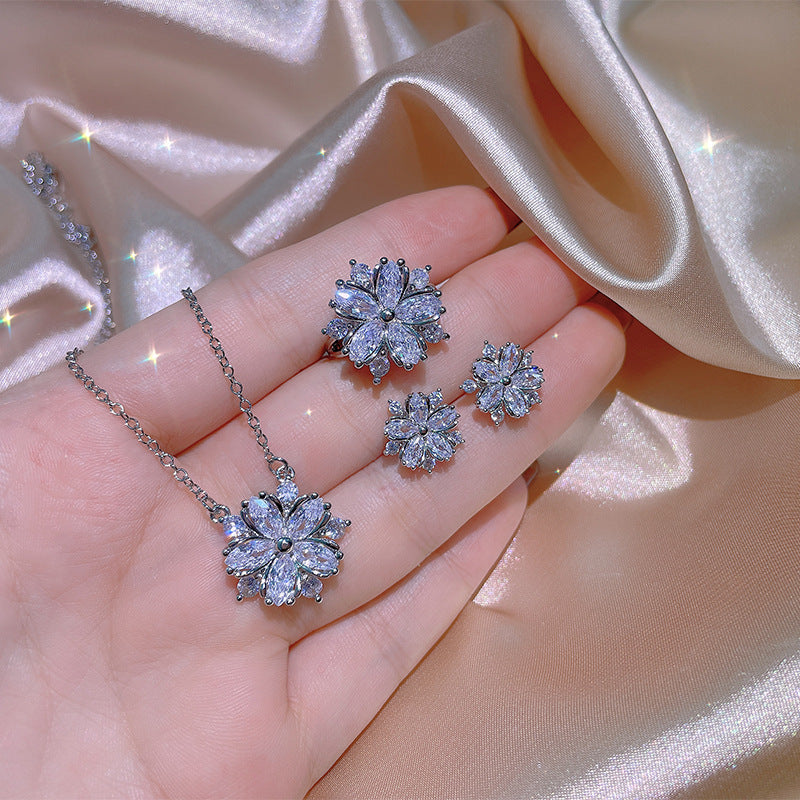 Silver jewelry set with floral designs on a hand against a satin background