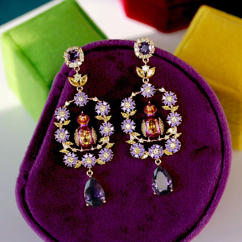 Ornate earrings with purple stones on a purple cushion