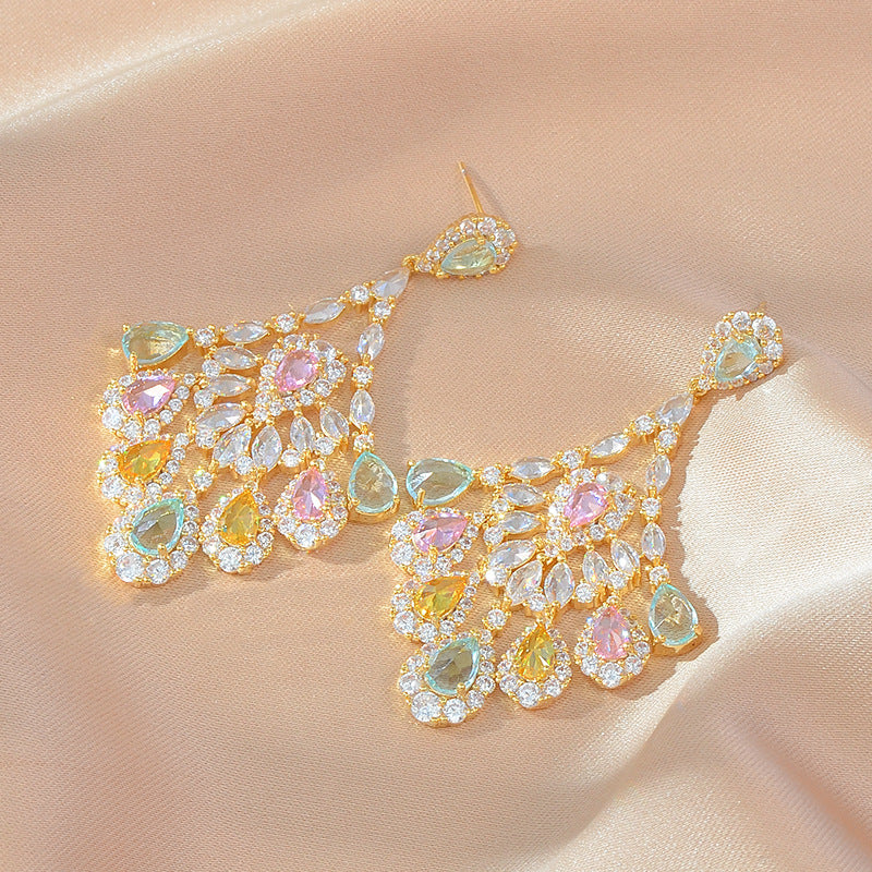 Pair of ornate earrings with multicolored gemstones on a beige fabric background