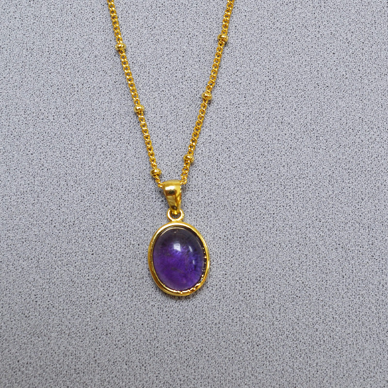 Gold necklace with a purple pendant on a gray background