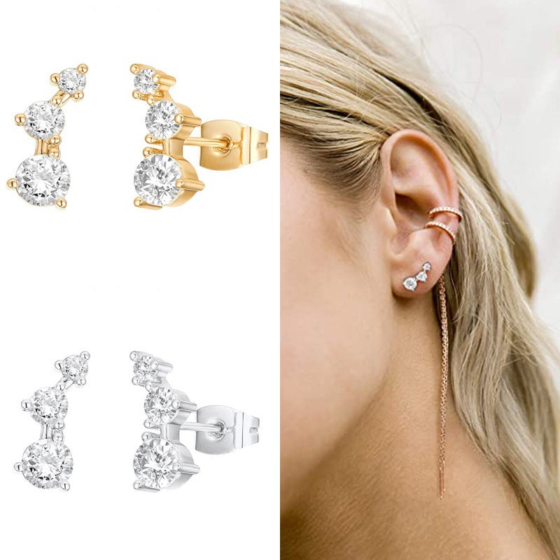 Gold and silver earrings with clear gemstones, shown on an ear and a plain background.