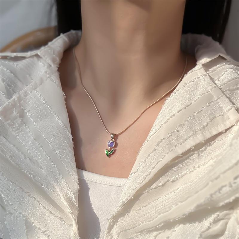 Necklace with a floral pendant worn by a person in a white textured garment.