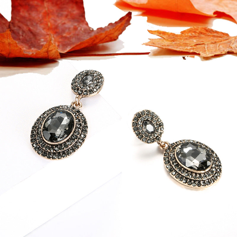 Pair of ornate earrings with gemstones on a white background with autumn leaves.